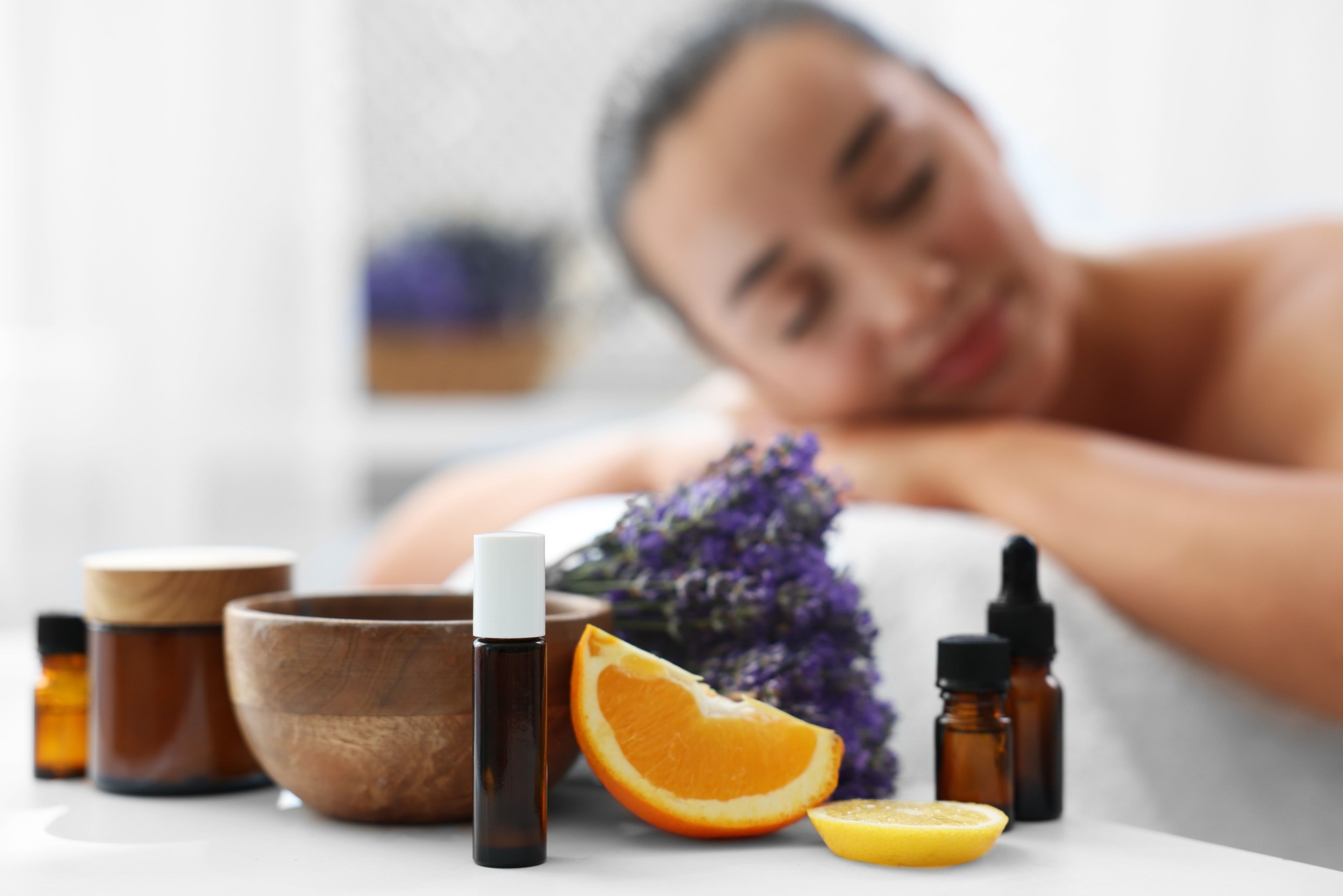 Woman relaxing on massage couch and bottles of essential oil with ingredients on table in spa salon, selective focus